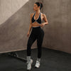 Eine Frau modelliert ein schwarzes Sport-BH und Leggings-Set mit Kontrastrand gegen eine neutrale graue Wand.