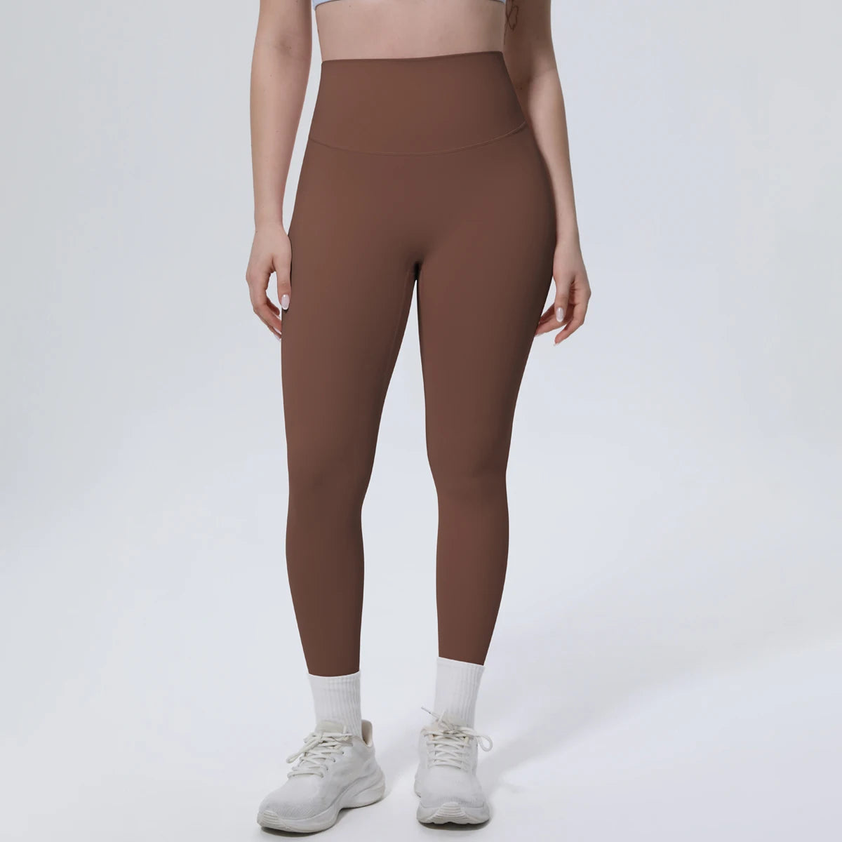 A model wearing high-waisted, full-length, mocha brown quick-drying yoga and fitness leggings and white sneakers.
