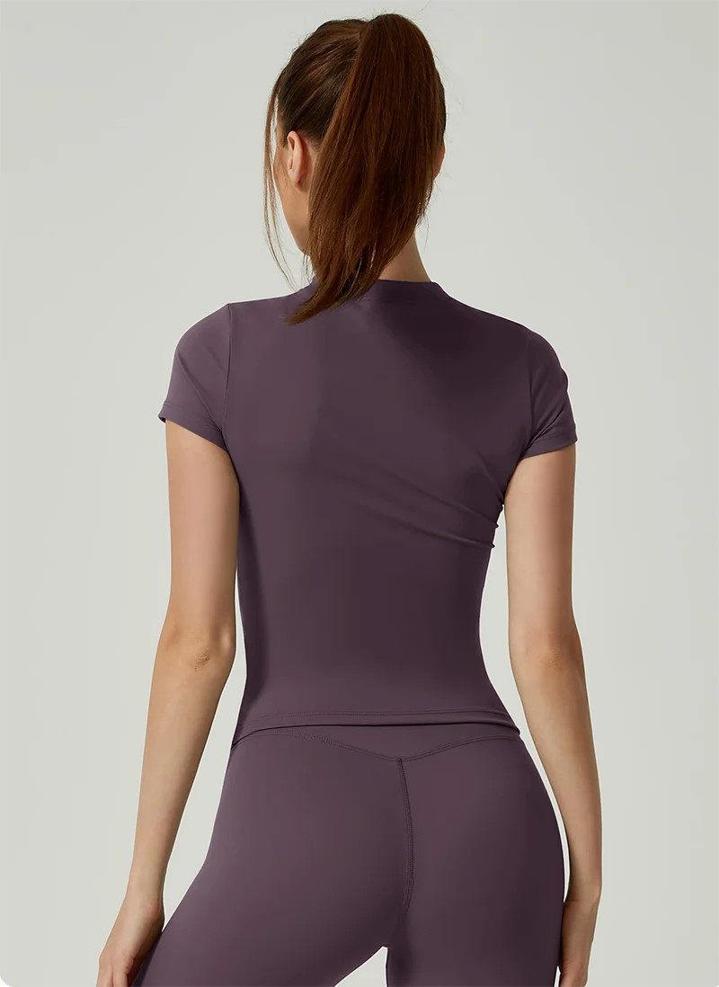 Una mujer vistiendo un conjunto de yoga de cintura alta color malva, top y leggings, vista desde atrás.