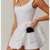Model in a white performance tennis dress with sleeveless top and pleated skirt.