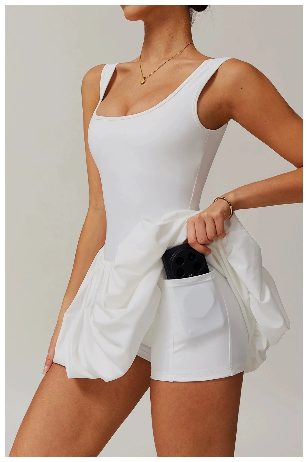 Model in a white performance tennis dress with sleeveless top and pleated skirt.