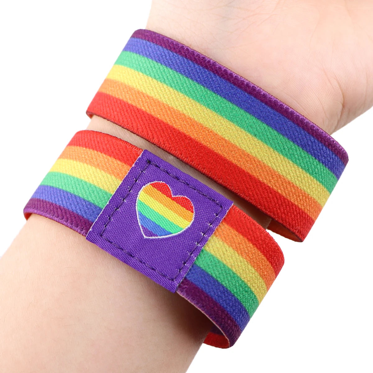A colorful LGBT stretch wristband bracelet featuring a rainbow stripe and a heart design on a person's wrist.