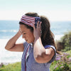 A woman wearing a red, white, and blue striped USA flag tube bandana and head wrap, looking out at the ocean.
