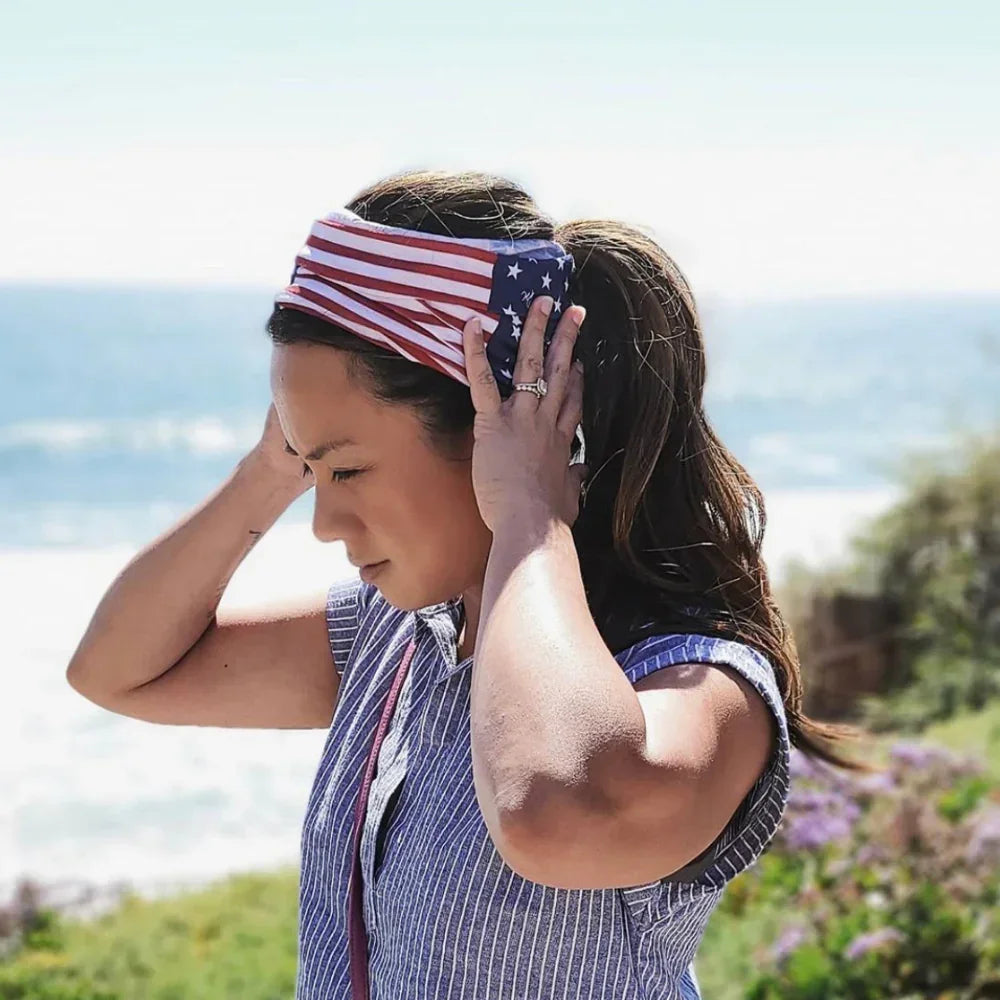 A woman wearing a red, white, and blue striped USA flag tube bandana and head wrap, looking out at the ocean.
