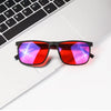A pair of red-tinted blue light blocking glasses resting on a white laptop keyboard.