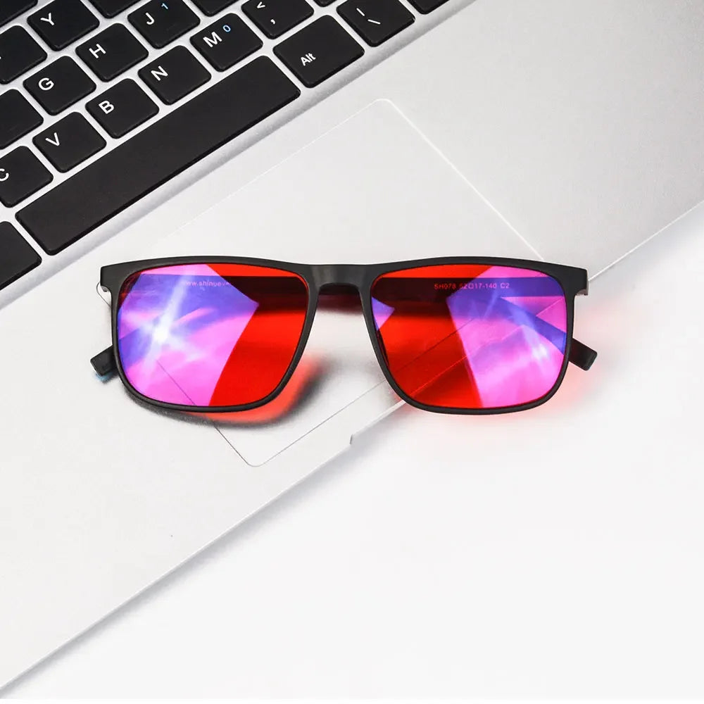 A pair of red-tinted blue light blocking glasses resting on a white laptop keyboard.