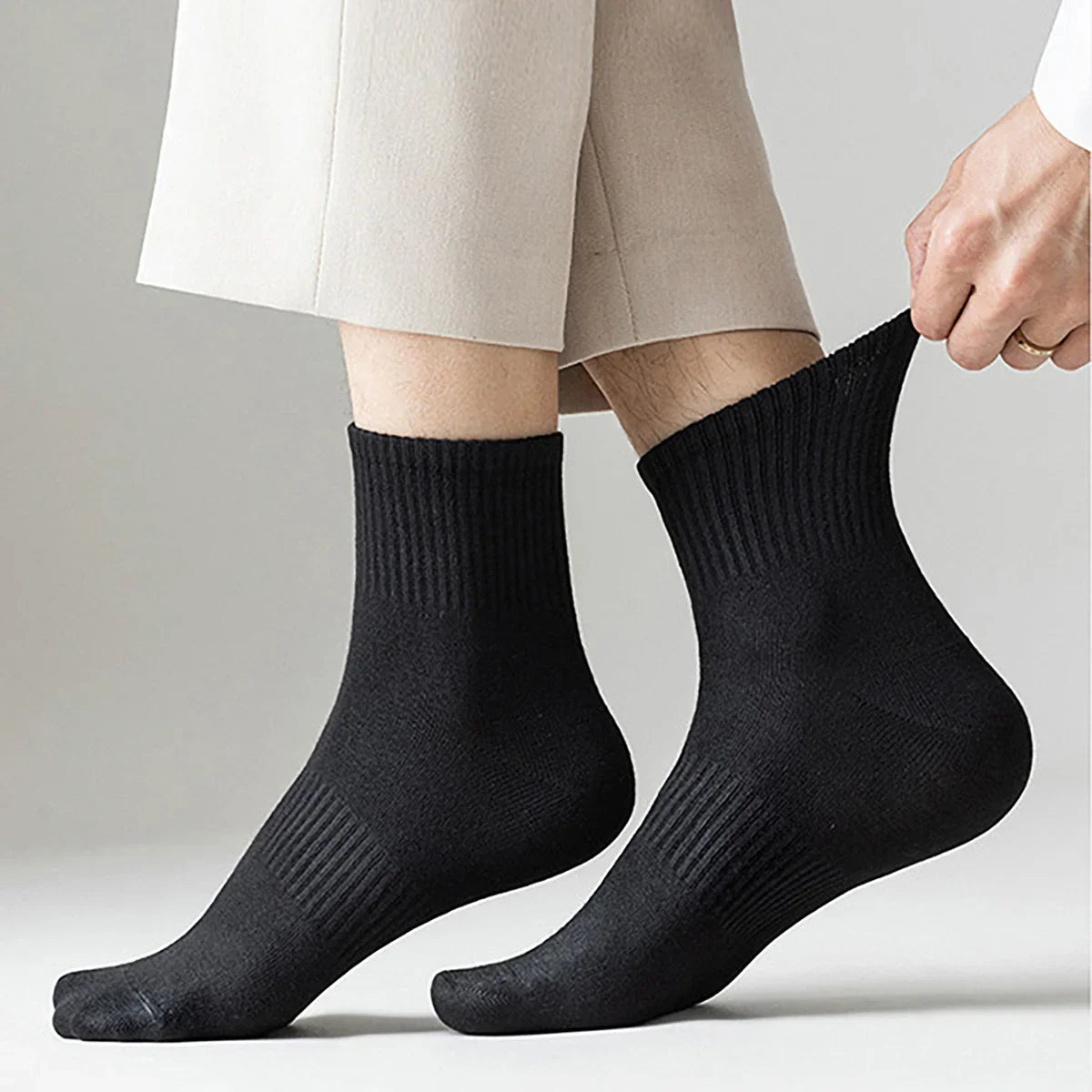A pair of black athletic crew socks being held by a hand, shown against a light background.