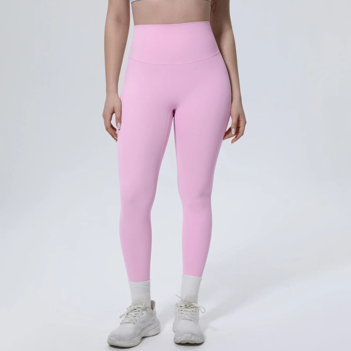 A model wears high-waisted pink quick-drying yoga and fitness leggings with white socks and gray athletic shoes.