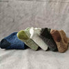 A collection of nine merino wool hiking socks in various earthy and cool tones laid out on a gray fabric.