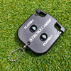A black portable golf score counter with a chain attached, lying on green grass.