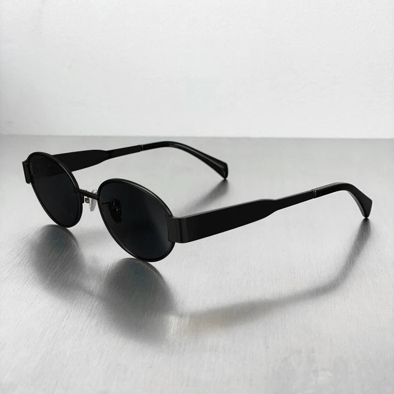 A pair of classic oval metal sunglasses in black resting on a light gray surface.
