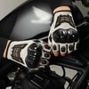 Nahaufnahme einer Hand mit schwarz-beige Schutzhandschuhen, die auf einem dunklen Motor- oder Fahrzeugteil ruht.