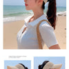A woman wearing a beige breathable anti-UV adjustable sun hat outdoors near the sea.