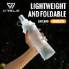 A hand holds a clear, lightweight and foldable silicone water flask with a white cap against a dark outdoor background.