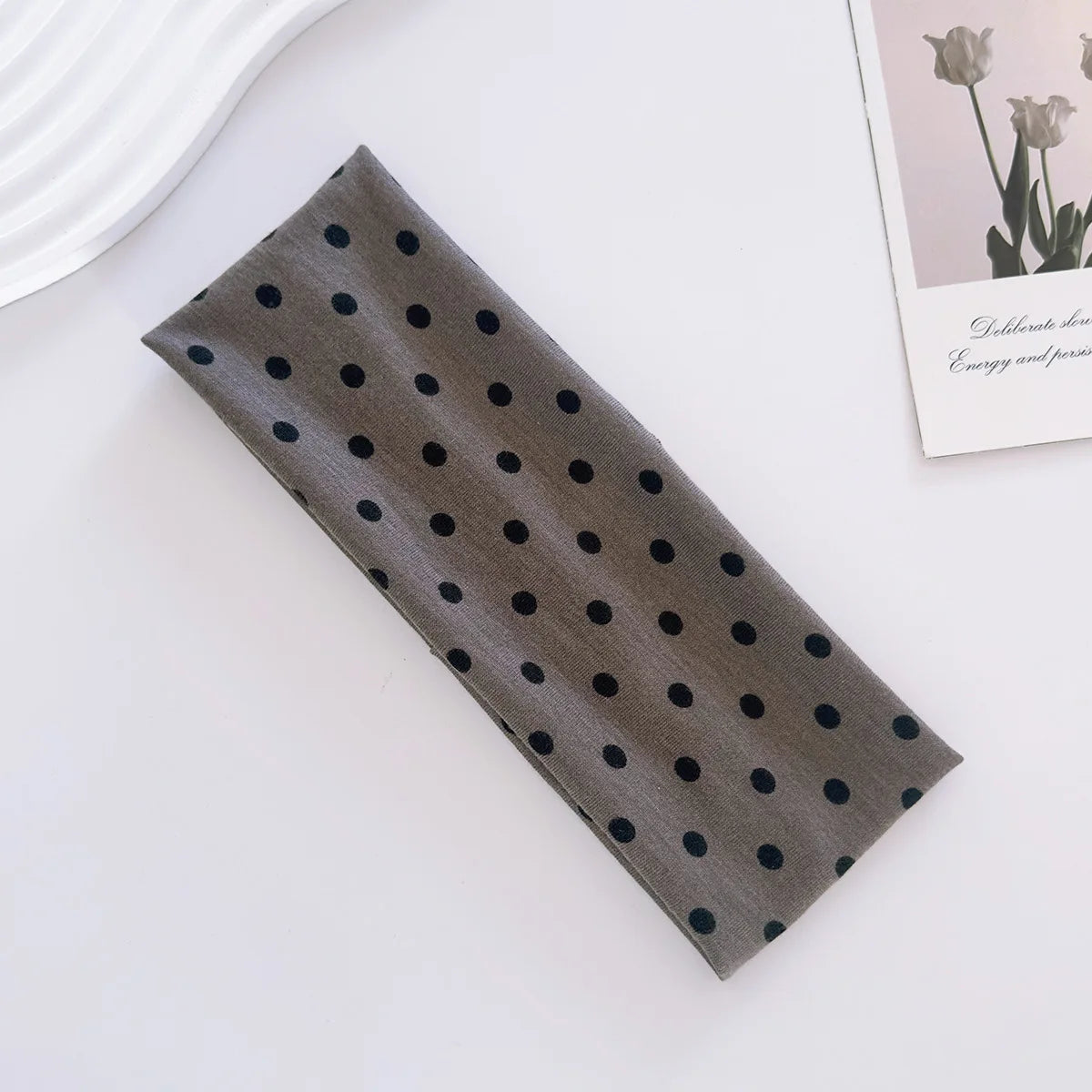 Un bandeau de yoga élastique à pois gris foncé posé sur une surface blanche.