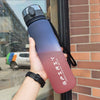 Eine Hand hält eine gradiente isolierte Wasserflasche in rosa und lila Tönen vor einem Ziegelwandhintergrund.