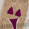 A purple two-piece bikini set with white trim is displayed on a beige woven mat.