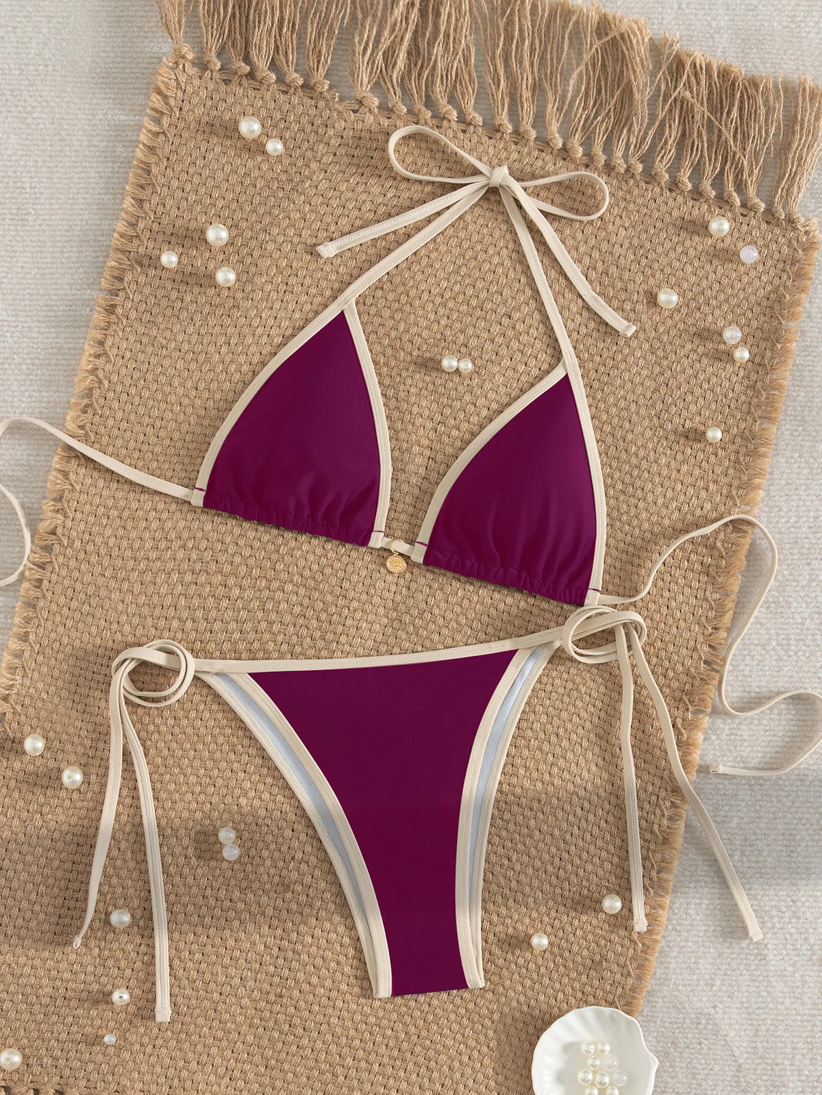 A purple two-piece bikini set with white trim is displayed on a beige woven mat.