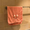 A pink coral fleece face towel with a cute bunny face design hanging on a metal rack.