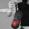 A hand holds a black pouch designed like a spider web, featuring red and black patterns, attached to a keychain.