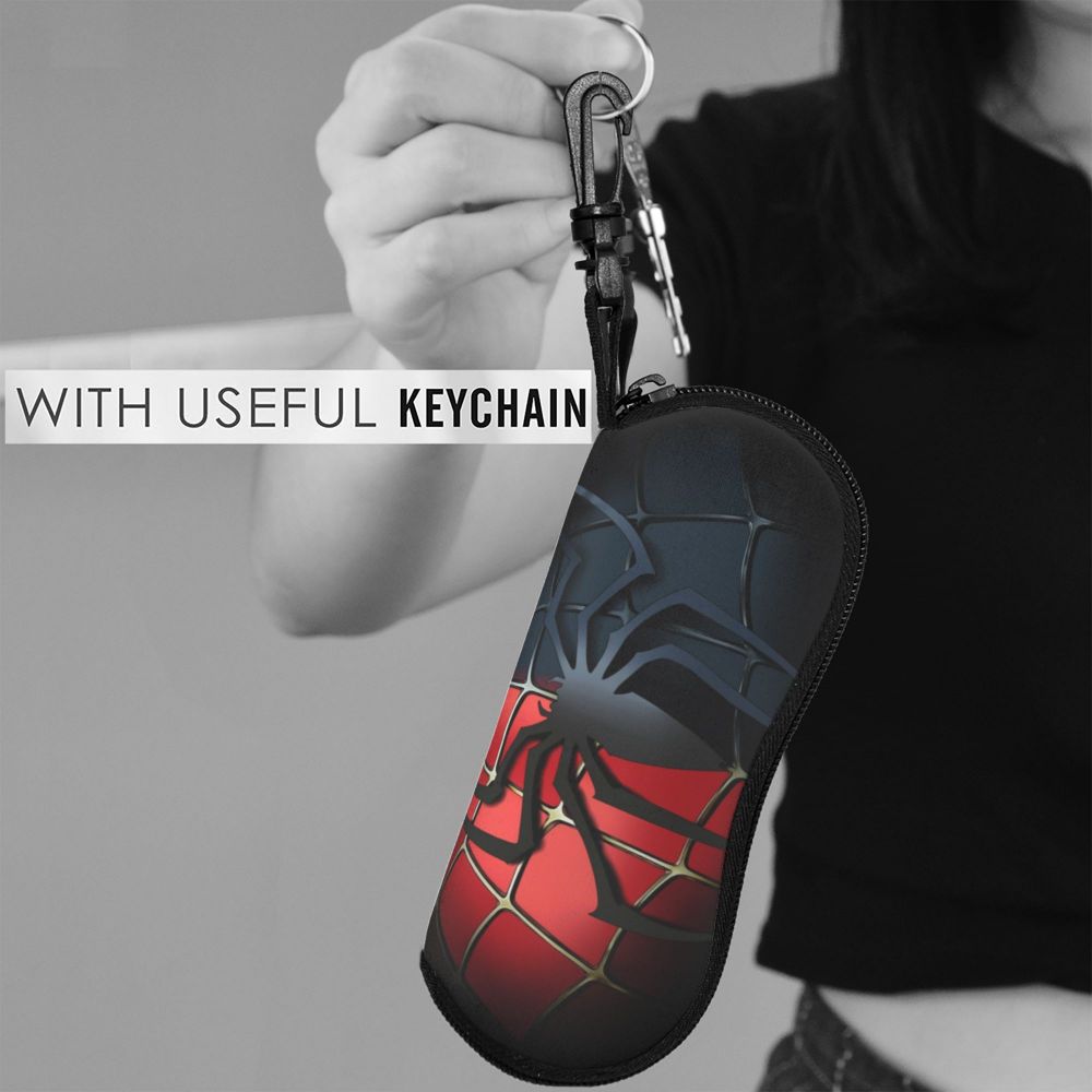 A hand holds a black pouch designed like a spider web, featuring red and black patterns, attached to a keychain.