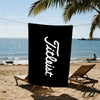 A black beach towel with the word 'Tiltless' written in white script is hanging on a line near the ocean.