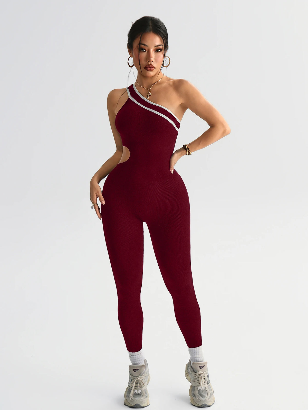 A model wearing a maroon seamless yoga jumpsuit with white trim, posing against a light gray background.