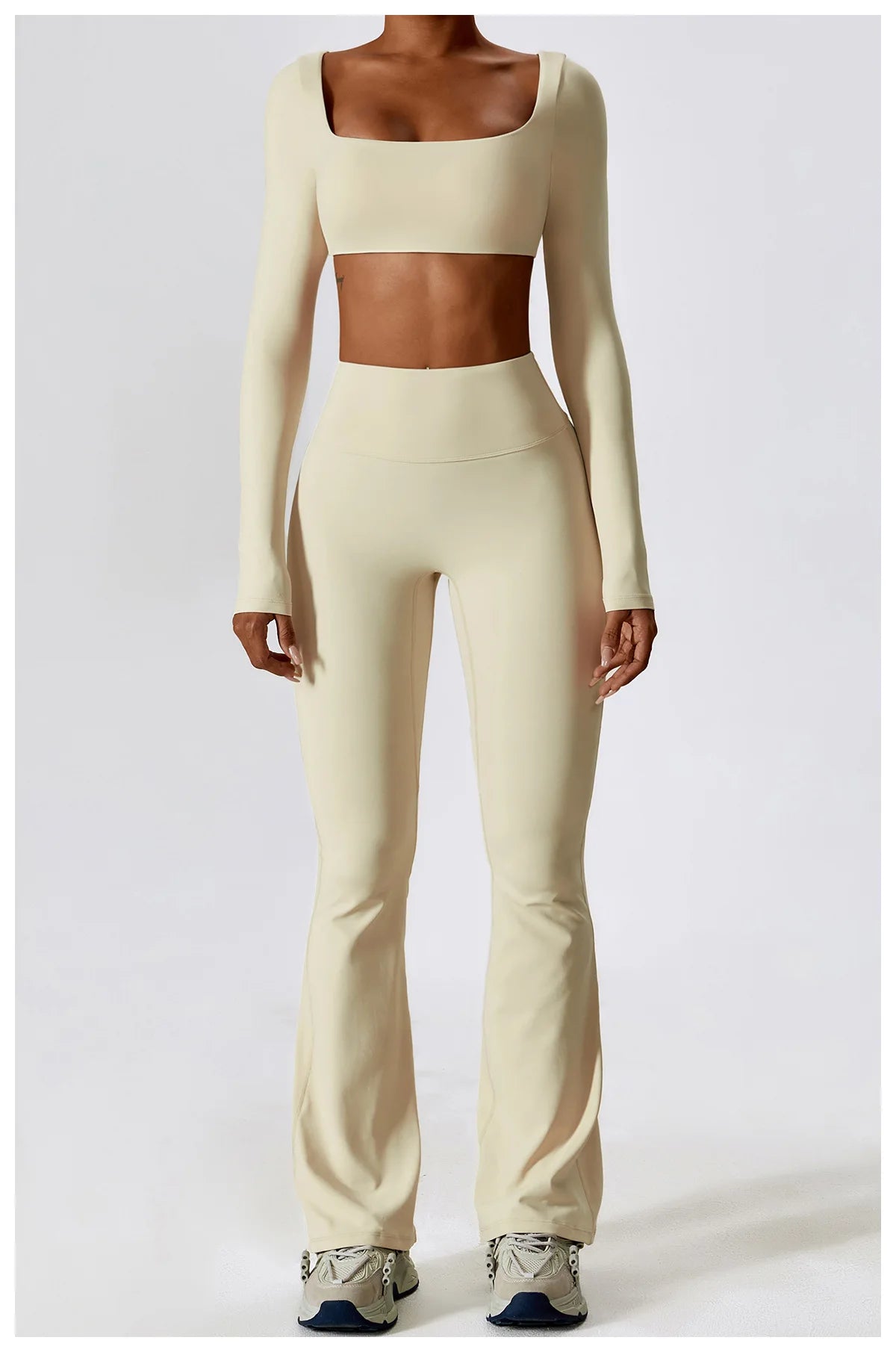 A woman models a beige women's performance tracksuit set consisting of a cropped top and matching full-length pants.