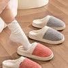 A close-up of water-proof plush fleece slippers in white, gray, and pink colors resting on a wooden floor.