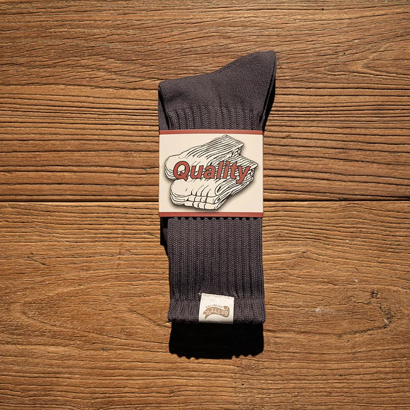 A pair of dark gray tube socks with a white label featuring the word Quality