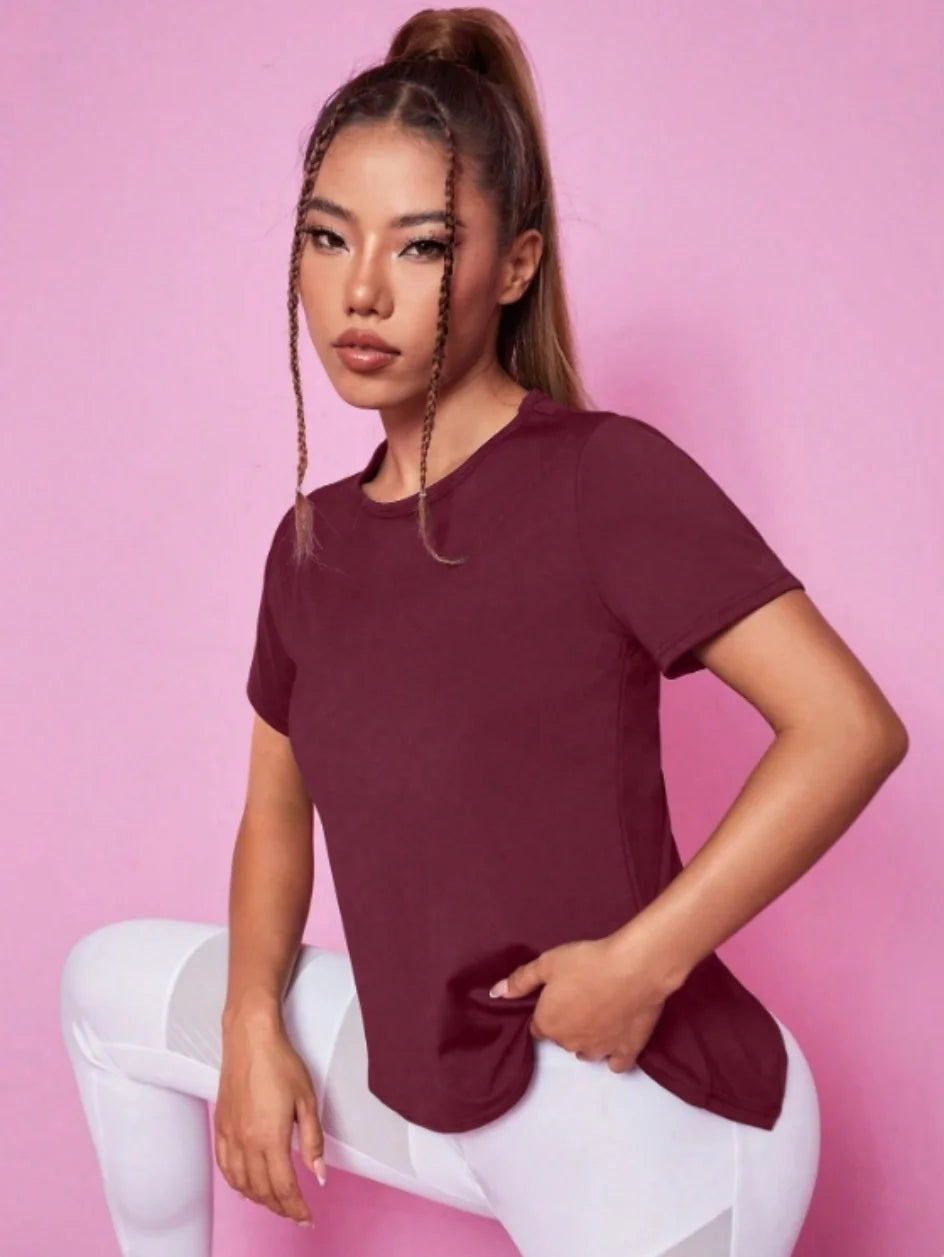 A woman wearing a maroon breathable summer yoga and fitness t-shirt in a studio setting.
