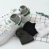 Un par de zapatillas deportivas blancas con calcetines grises y verdes sobre un fondo de cuadrícula.