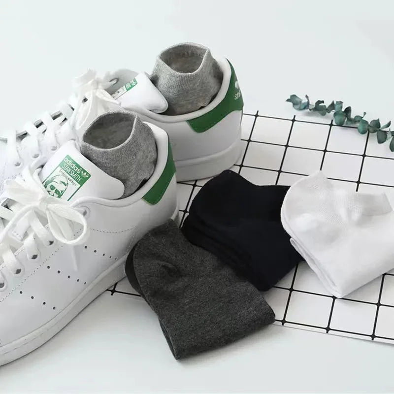 Un par de zapatillas deportivas blancas con calcetines grises y verdes sobre un fondo de cuadrícula.