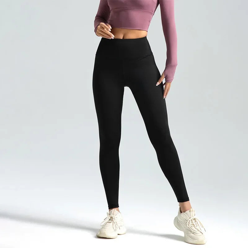 A woman wearing black seamless high-waist yoga leggings and a mauve top standing in a studio setting.