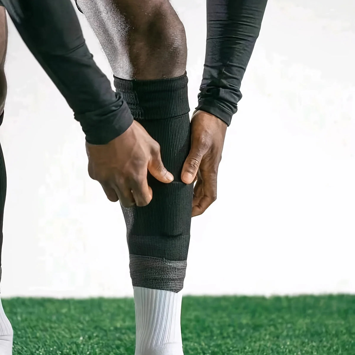 A person is applying or adjusting a black compression sleeve on another person's leg during football practice.
