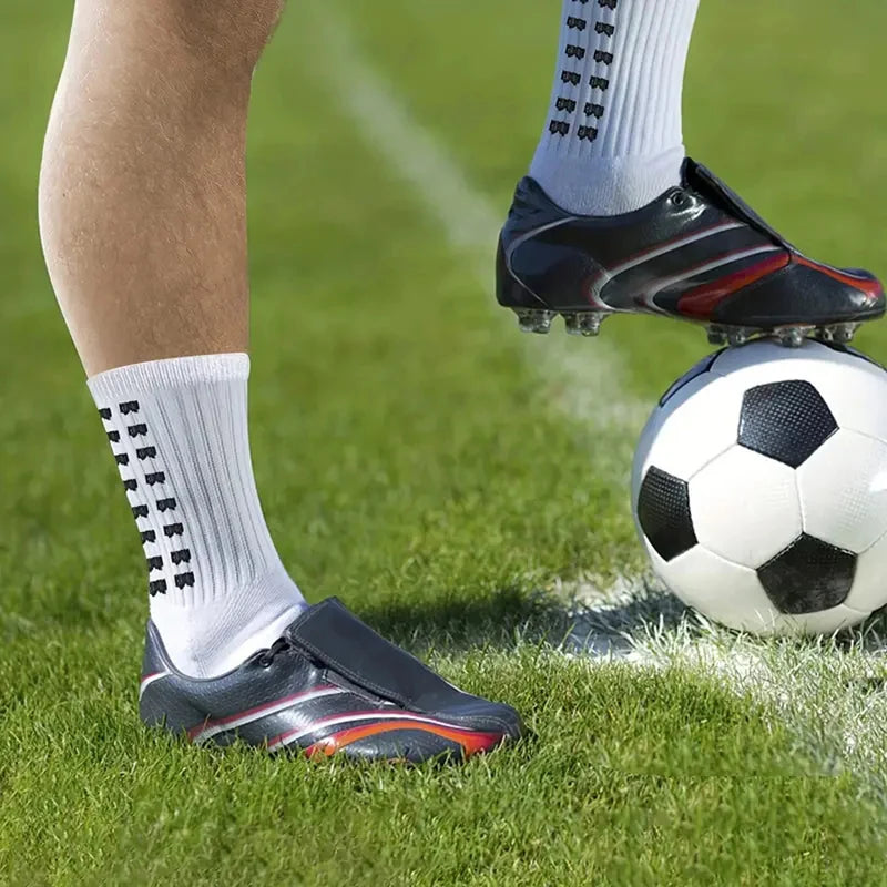 A close-up of a person's leg wearing non-slip silicone sports socks and cleats on a green football field.