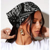 Una mujer vistiendo un pañuelo triangular bohemio paisley negro y blanco con aretes de aro dorados.
