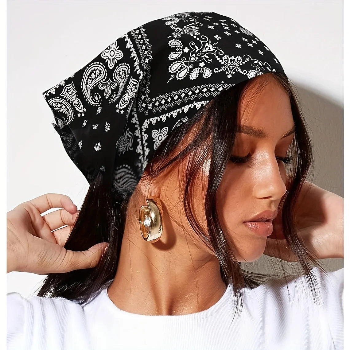 Una mujer vistiendo un pañuelo triangular bohemio paisley negro y blanco con aretes de aro dorados.