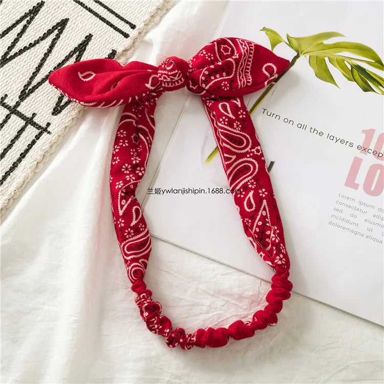 Un bandeau bohème à motif paisley rouge noué en nœud, posé sur un tissu blanc.