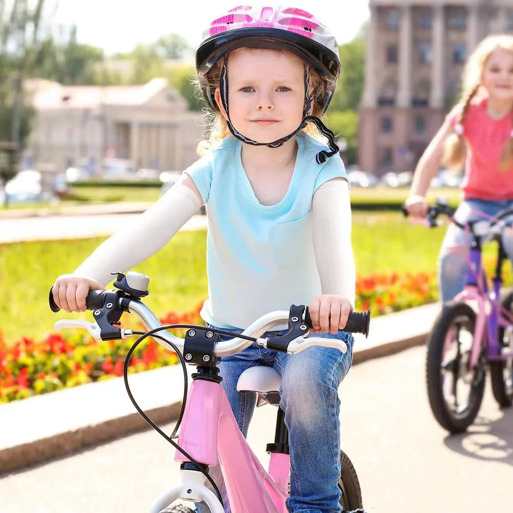 Una niña viste un casco rosa y una camiseta azul, montando una bicicleta rosa al aire libre.