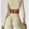 A model wearing a beige long-sleeved crop top and matching high-waisted leggings from a women's performance tracksuit set.