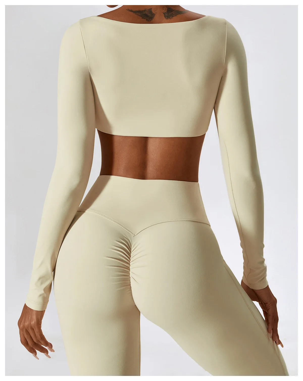 A model wearing a beige long-sleeved crop top and matching high-waisted leggings from a women's performance tracksuit set.
