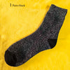 A pair of black merino wool hiking socks displayed on a yellow fabric background.