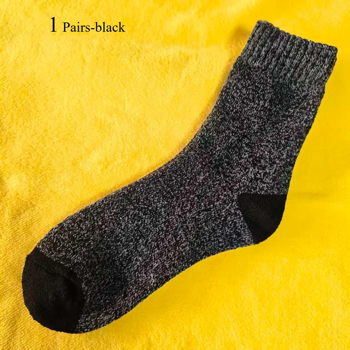 A pair of black merino wool hiking socks displayed on a yellow fabric background.