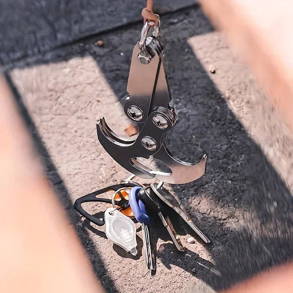 Stainless steel folding grappling hook with various tools resting on a dark surface.