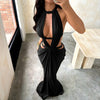 A woman wearing an elegant black maxi dress with a draped cut-out back, standing indoors.