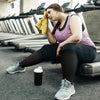 A woman wearing compression socks is sitting on a gym floor with various exercise equipment in the background.