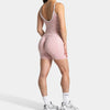 A woman models pink seamless yoga shorts and a matching tank top with white sneakers.