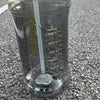 A clear insulated sports water bottle filled with water, resting on an asphalt surface.