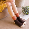 A close-up of a person's legs and feet wearing knitted crew socks in shades of orange, brown, and beige.